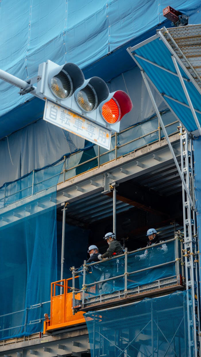 Construction workers visible on a building site in Kamakura, Japan, next to a red traffic light.