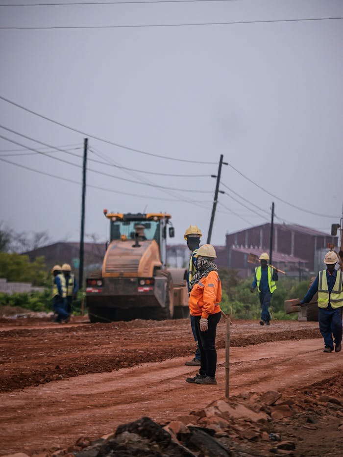 Construction workers at a road site operating heavy machinery, ensuring safety standards.